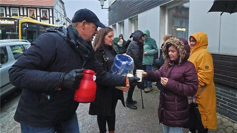 Der GZ-Schweinchenverkauf läuft in Goslar auf Hochtouren Mehrere Personen in Winterkleidung stehen auf einem Gehweg vor einem Gebäude, eine Person reicht einer anderen einen Becher, eine weitere hält eine rote Thermoskanne