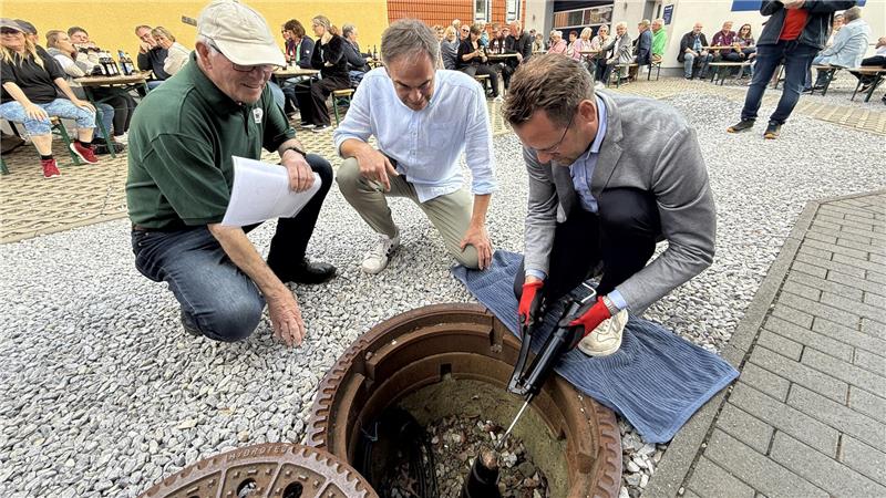 Drei Männer knien vor einem Loch im Boden, aus dem ein Stück Metall herausragt. Einer drückt Fett aus einer Speitze auf die Konstruktion. 