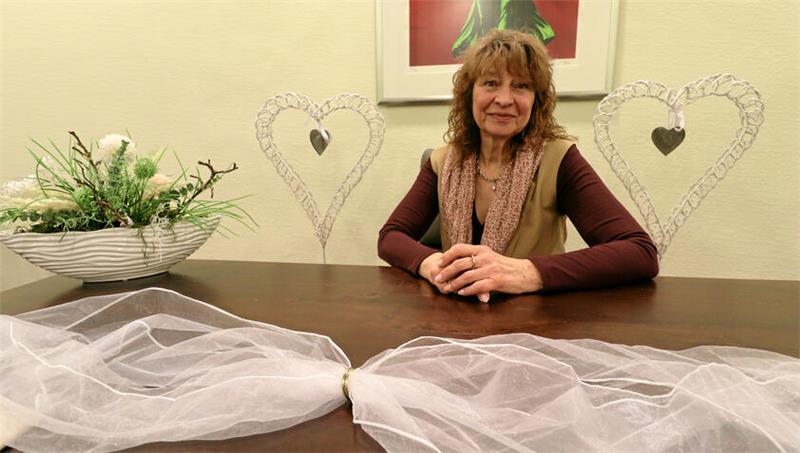 Eine Frau sitzt an einem geschmückten Tisch, im Hintergrund stehen Herzaufsteller.