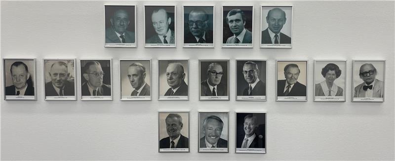 Die Deutschen nehmen die Entnazifizierung in eigene Hände Wand mit 18 schwarz-weißen Porträtfotos von Personen in formeller Kleidung, angeordnet in drei Reihen.