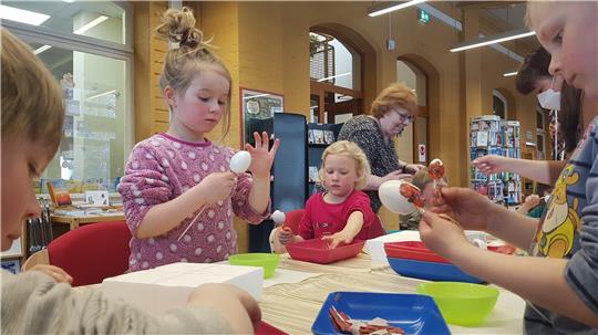 Gar nicht so einfach, wie es aussieht: Nach dem Vorlesen bekleben die Kinder Ostereier mit bunten Papierschnitzeln. Petra Westphal (4. v. li.) vom Jugendring unterstützt tatkräftig.