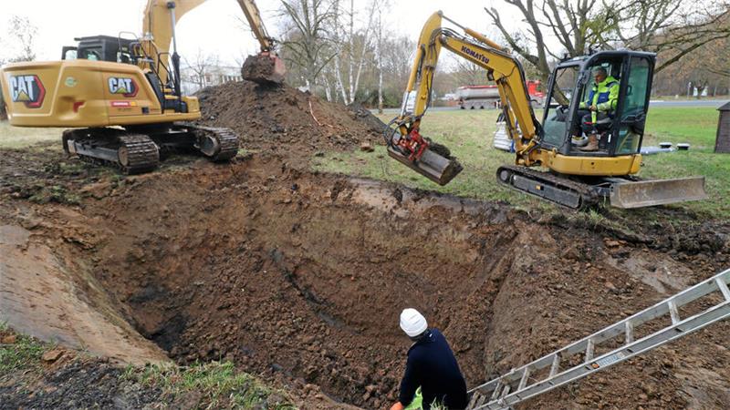 Zwei Bagger an einem großen Loch, in das eine Leiter hineinführt.