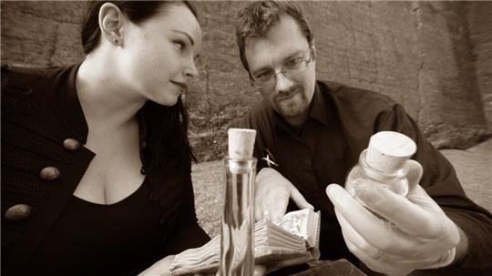 Zwei Personen sitzen an einem Tisch mit mehreren Flaschen und einem Stapel Geldscheine