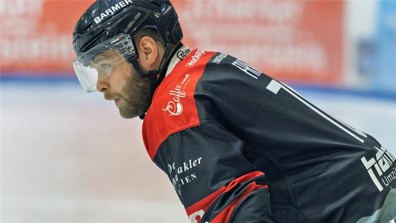 Eishockeyspieler in schwarzem und rotem Trikot mit Helm in Spielhaltung auf dem Eis-