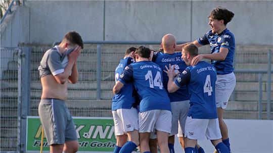 Fußballspieler in blauen Trikots feiern auf dem Spielfeld, während ein Spieler in grauem Trikot mit den Händen das Gesicht bedeckt steht
