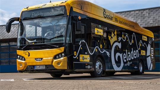 Gelb-schwarzer Elektrobus mit der Aufschrift 'Goslar Wir sind elektrisch' und 'Geladen' steht vor einem Gebäude