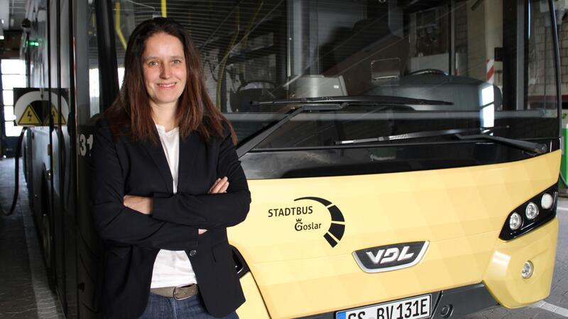 Frau mit verschränkten Armen steht vor gelbem Stadtbus der Marke VDL in einer Garage