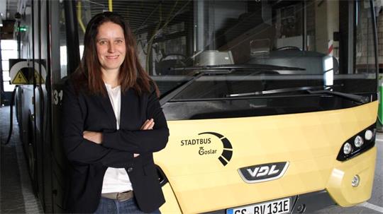 Frau mit verschränkten Armen steht vor gelbem Stadtbus der Marke VDL in einer Garage