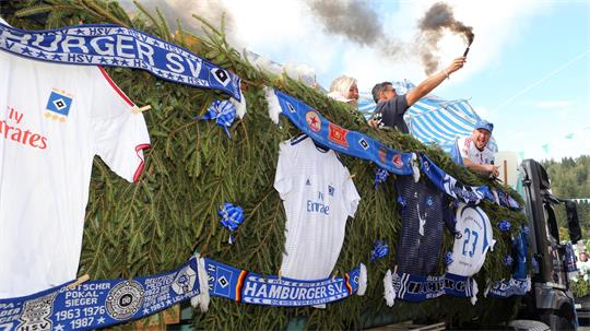 Mit Tannenzweigen geschmückter Wagen mit Hamburger-SV-Trikots und Fans, einer hält eine rauchende Fackel hoch.