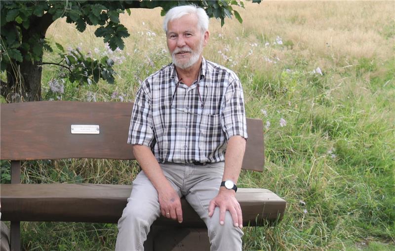 Ein Mann sitzt auf einer Bank im Grünen.