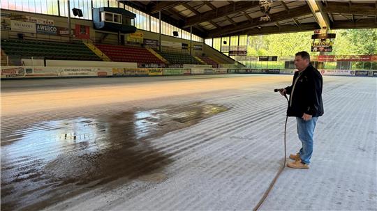 Geschäftsführer Dirk Becker spritzt mit dem Gartenschlauch Wasser auf den gefrorenen Beton im Eisstadion.