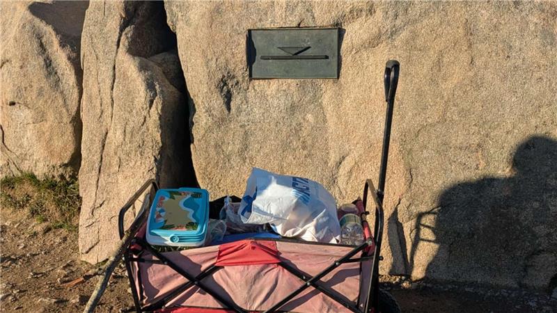 Ein gefüllter Bollerwagen steht vor einer Steinwand.