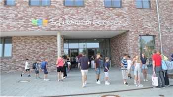 Schülerinnen und Schüler stehen im Sommer vor dem Eingang des riesigen Schulzentrums Goldene Aue.