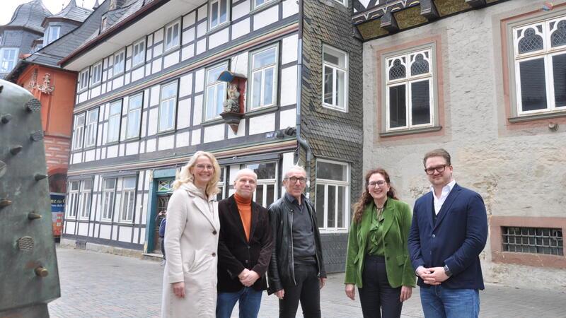 Fünf Personen stehen vor einem Fachwerkhaus und einem Gebäude mit Sandsteinfassade in einer Altstadt
