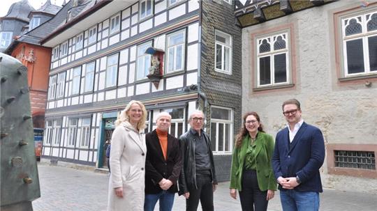 Fünf Personen stehen vor einem Fachwerkhaus und einem Gebäude mit Sandsteinfassade in einer Altstadt
