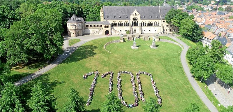 Gestellter Glückwunsch zum Jubiläum: Zu Füßen der Pfalz bilden mehr als 650 Schüler von Schiller-, Goethe- und Grundschule Oker im Mai des Vorjahres den runden Stadtgeburtstag ab. Diese Aufnahme schmückt jetzt den Band mit den Bildern, die Kinder von ihren Goslarer Lieblingsorten gemalt haben. Foto: Ritter/ Stadt Goslar