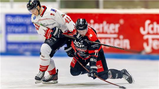 Ein Eishockeyspieler in Weiß und ein Eishockeyspieler in Schwarz und Rot kämpfen um den Puck.