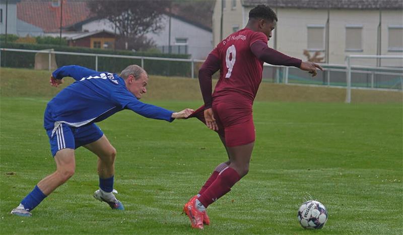 Zwei Fußballspieler auf dem Spielfeld, einer in rotem Trikot mit der Nummer 9 läuft mit dem Ball, der andere in blauem Trikot versucht ihn zu stoppen