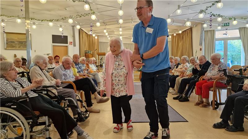 Gisela Ose (101) präsentiert eine geblümte Bluse und eine rosafarbene Weste. In der letzten Runde meistert sie den Laufsteg ohne ihren Rollator und lässt sich stattdessen von Frank Lassig führen.