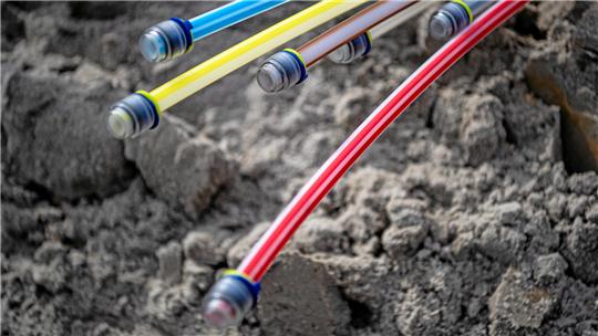 Das Foto zeigt bunte Glasfaserkabel in der Erde.