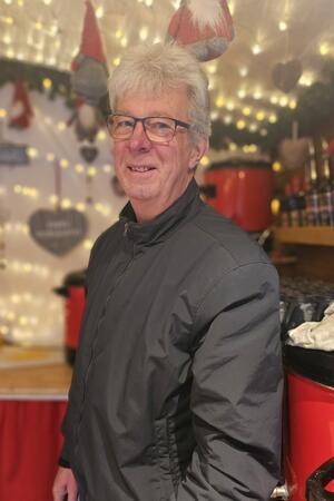 Am Super-Samstag kommen Besucher aus ganz Deutschland Person mit kurzen, hellen Haaren trägt eine schwarze Jacke und steht vor einem festlich beleuchteten Stand mit roten und schwarzen Dekorationen.