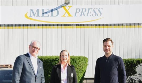 Drei Personen stehen vor einer Wand mit dem Schriftzug 'MED X PRESS'