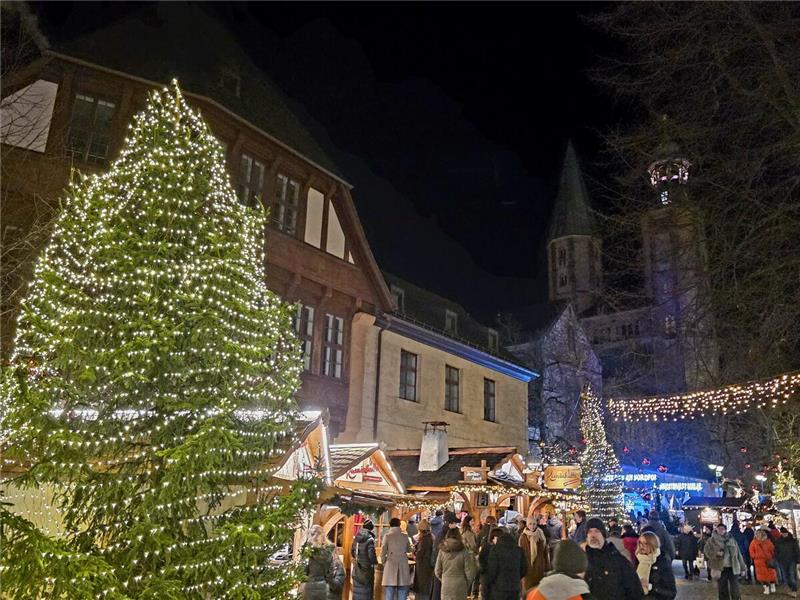 Ein beleuchteter Baum steht neben den stark besuchten Weihnachtsmarkt-Buden.