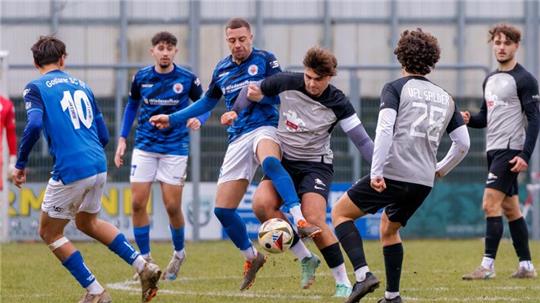 Fußballspiel mit mehreren Spielern in blauen und schwarz-weißen Trikots, ein Spieler tritt den Ball.