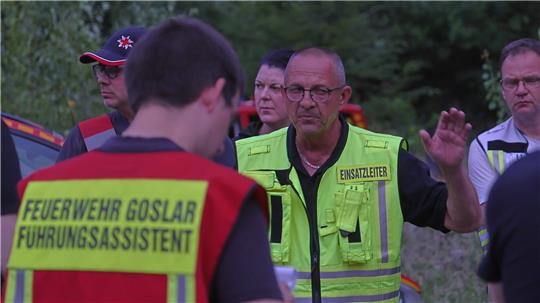 Sechs Personen stehen nebeneinander in einem Raum mit großen Fenstern, drei in Uniform halten Urkunden in den Händen.