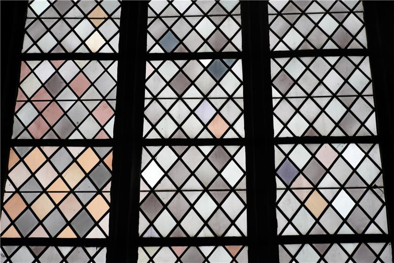 Graues Glas wird durch Sonneneinstrahlung leicht violett; die eher ockerfarbenen Flächen erklärt das nicht, sie sind später eingesetzt, vermutet der Glasermeister.