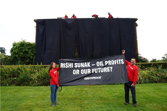 Greenpeace-Aktivisten mit einem Banner vor dem verhüllten Haus des britischen Premiers Rishi Sunak.