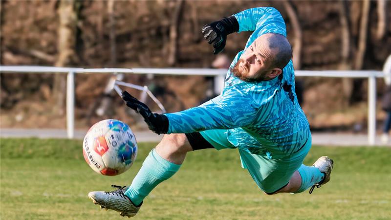Torwart in türkisfarbenem Trikot und Handschuhen springt auf dem Fußballfeld und versucht, einen Fußball abzuwehren