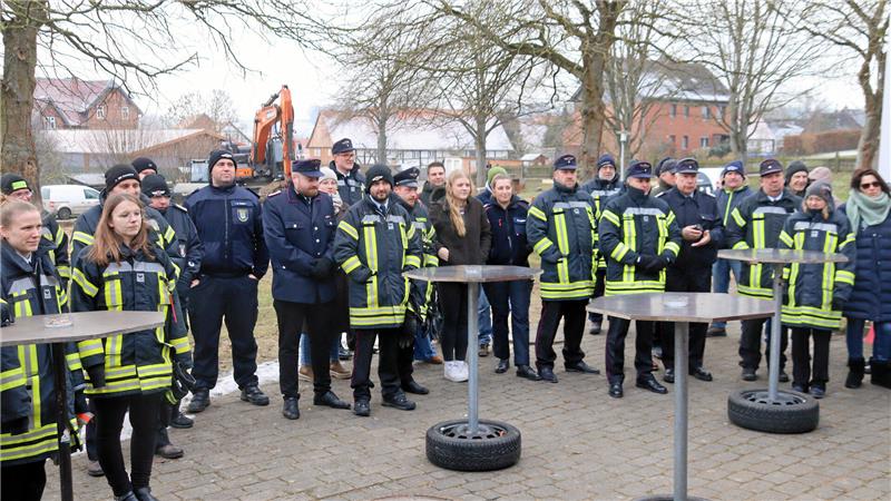 Zuschauer, viele davon in Feuerwehrkleidung, stehen an Stehtischen.