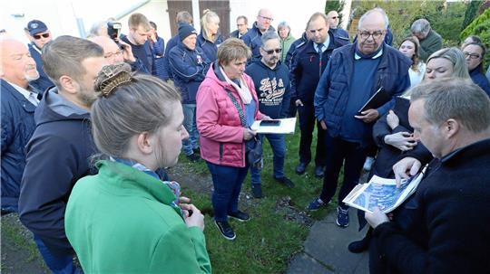Viele Personen stehen im Halbkreis um einen Mann mit Lageplan.