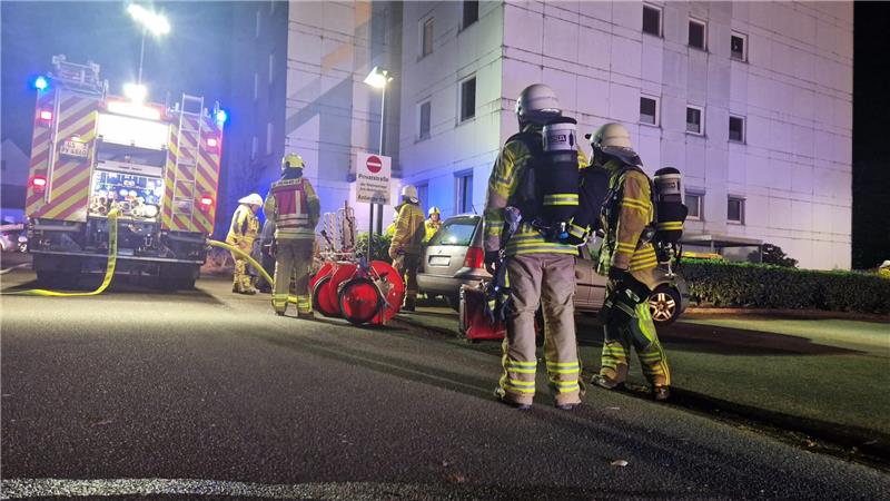 Feuerwehrleute stehen neben einem Feuerwehrauto, das vor dem betroffenen Häuserblock steht. Dort kam es zu einem Brand im 3. Obergeschoss. 