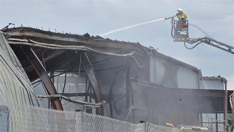 Feuerwehrmann in Schutzkleidung auf Drehleiter löscht Brand an beschädigtem Industriegebäude mit Wasserschlauch.
