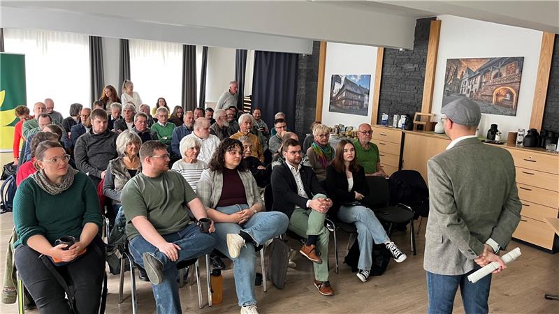 Ein Mann steht in einem Saal vor Publikum.