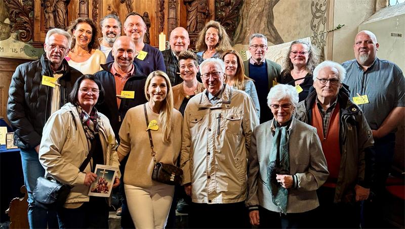 Gruppe von Menschen unterschiedlichen Alters mit Namensschildern im historischen Innenraum einer Kapelle mit Holzvertäfelung