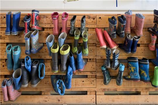 Gummistiefel hängen an der Palettenwand einer Kindertagesstätte in Halle (Saale). In Deutschland fehlen Erzieherinnen und Erzieher.