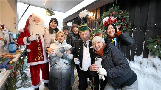 Ein Mann ist als Weihnachtsmann verkleidet und steht neben diversen Frauen winterlich gekleidet sind.