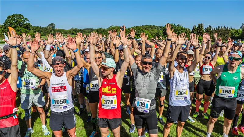 Menschen in bunter Laufkleidung stehen mit nach oben gestreckten Händen auf der Startlinie.