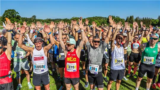 Menschen in bunter Laufkleidung stehen mit nach oben gestreckten Händen auf der Startlinie.