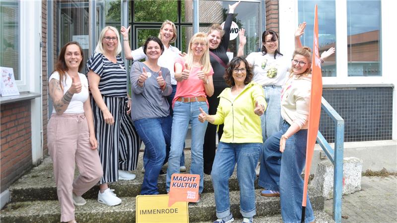 Gruppe vonneun Frauen vor einem Gebäude, einige winken, eine Person hält ein Schild mit der Aufschrift 'Macht Kultur'