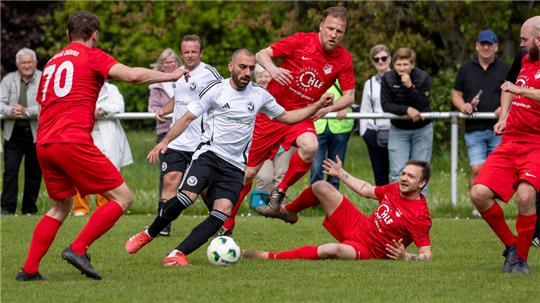 Fußballspiel mit Spielern in roten und weißen Trikots auf einem Spielfeld, ein Spieler in Weiß dribbelt den Ball, mehrere Spieler in Rot versuchen ihn zu stoppen.