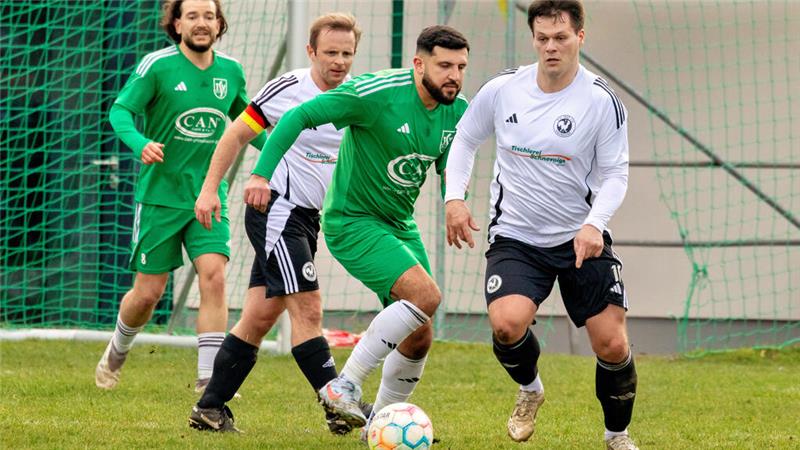 Vier Fußballspieler in grünen und weißen Trikots kämpfen um einen Ball vor einem Tor mit grünem Netz