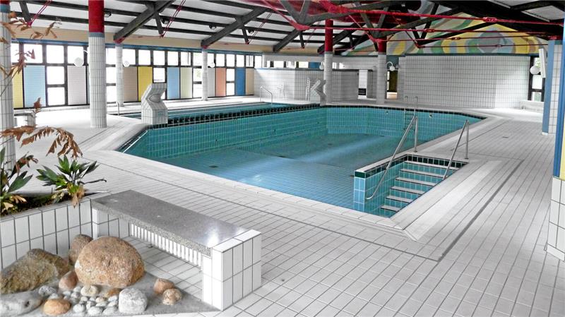 Innenaufnahme eines leeren Schwimmbeckens in einer Halle mit weißen Fliesen und großen Fenstern