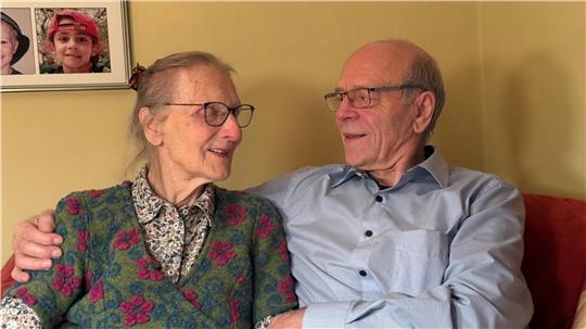 Älteres Ehepaar sitzt auf dem Sofa, schaut sich verliebt an und umarmt sich.