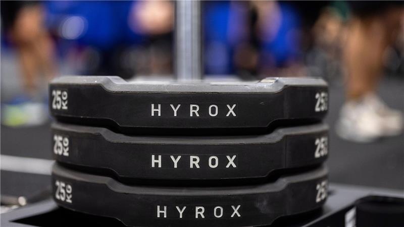 Hantelscheiben mit dem Schriftzug Hyrox an einem Messestand, wo wenig später ein Lauf- und Workout-Wettbewerb stattfinden sollte.