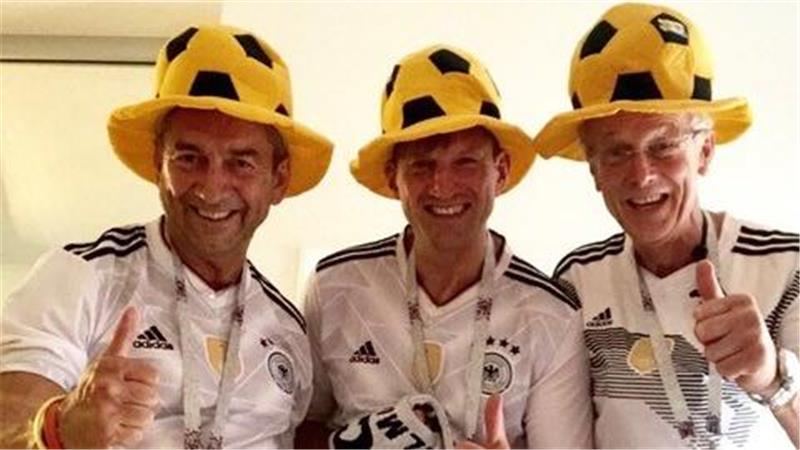 Drei Personen in Deutschland-Fußballtrikots und gelben Fußballhut mit Daumen hoch.
