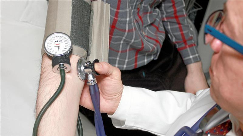 Das Bild zeigt einen Arzt, der bei einem Patienten den Blutdruck misst.